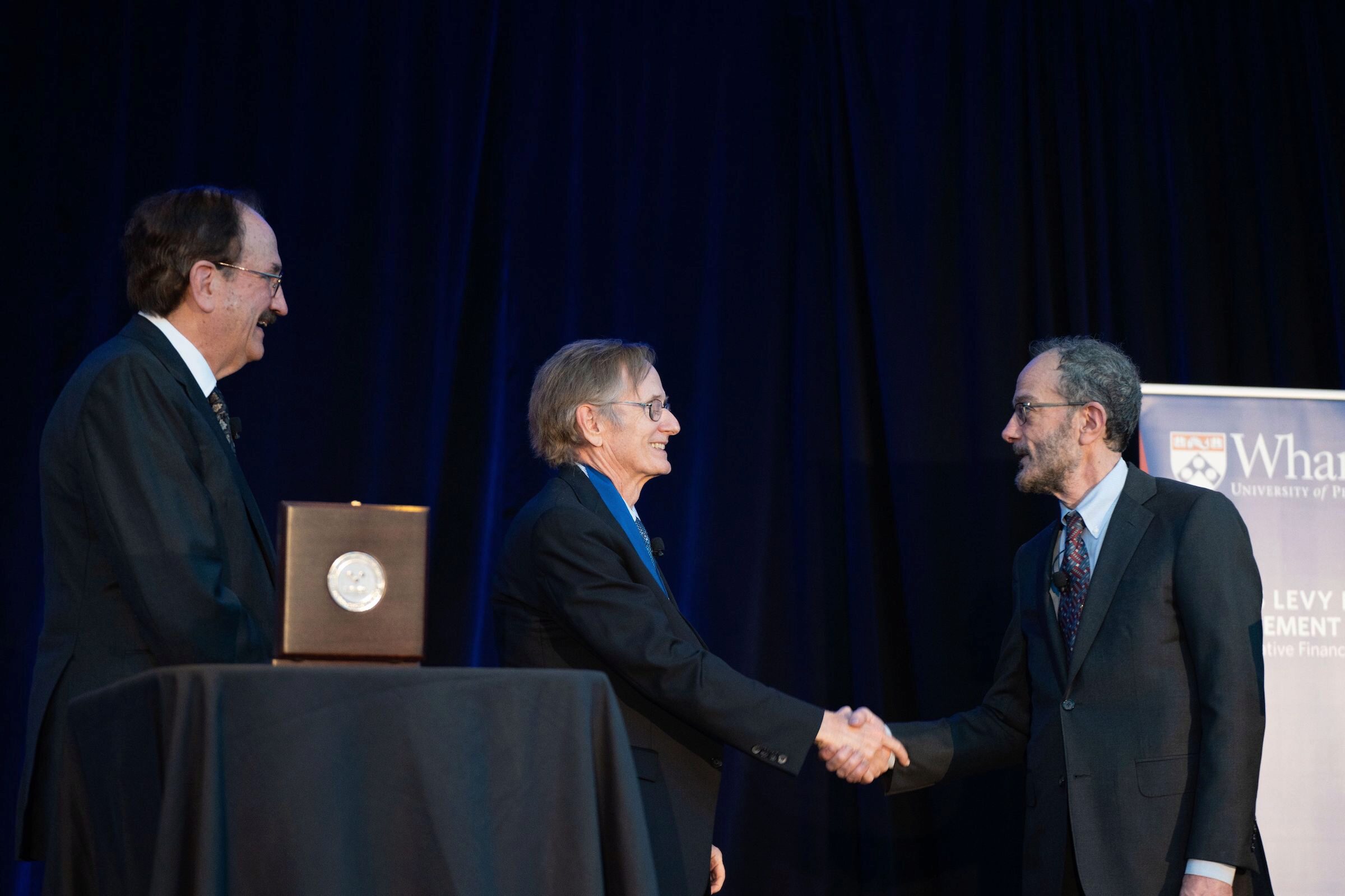 Albert S. “Pete” Kyle and Ken Levy shake hands as Bruce Jacobs watches with the Jacobs Levy Prize