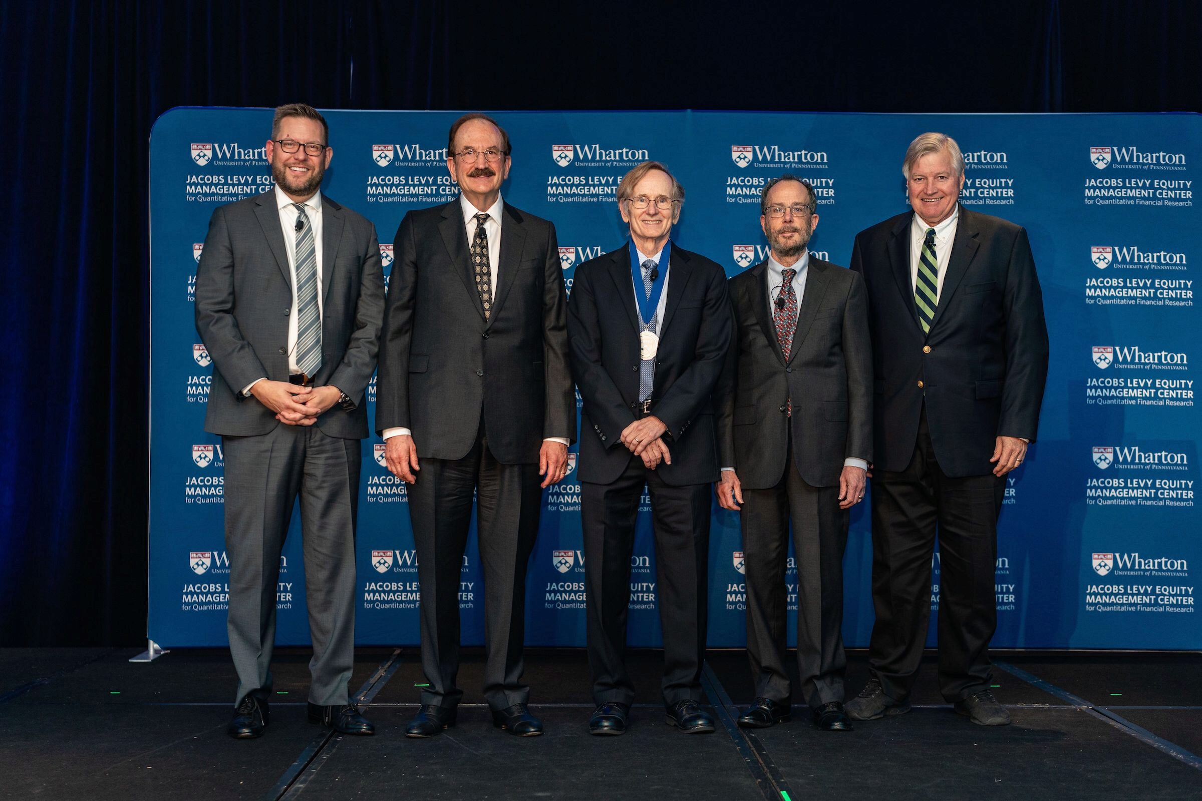 Albert S. “Pete” Kyle poses and smiles, wearing the Jacobs Levy Prize medal, between Christopher Geczy, Bruce Jacobs, Ken Levy, and Craig MacKinlay