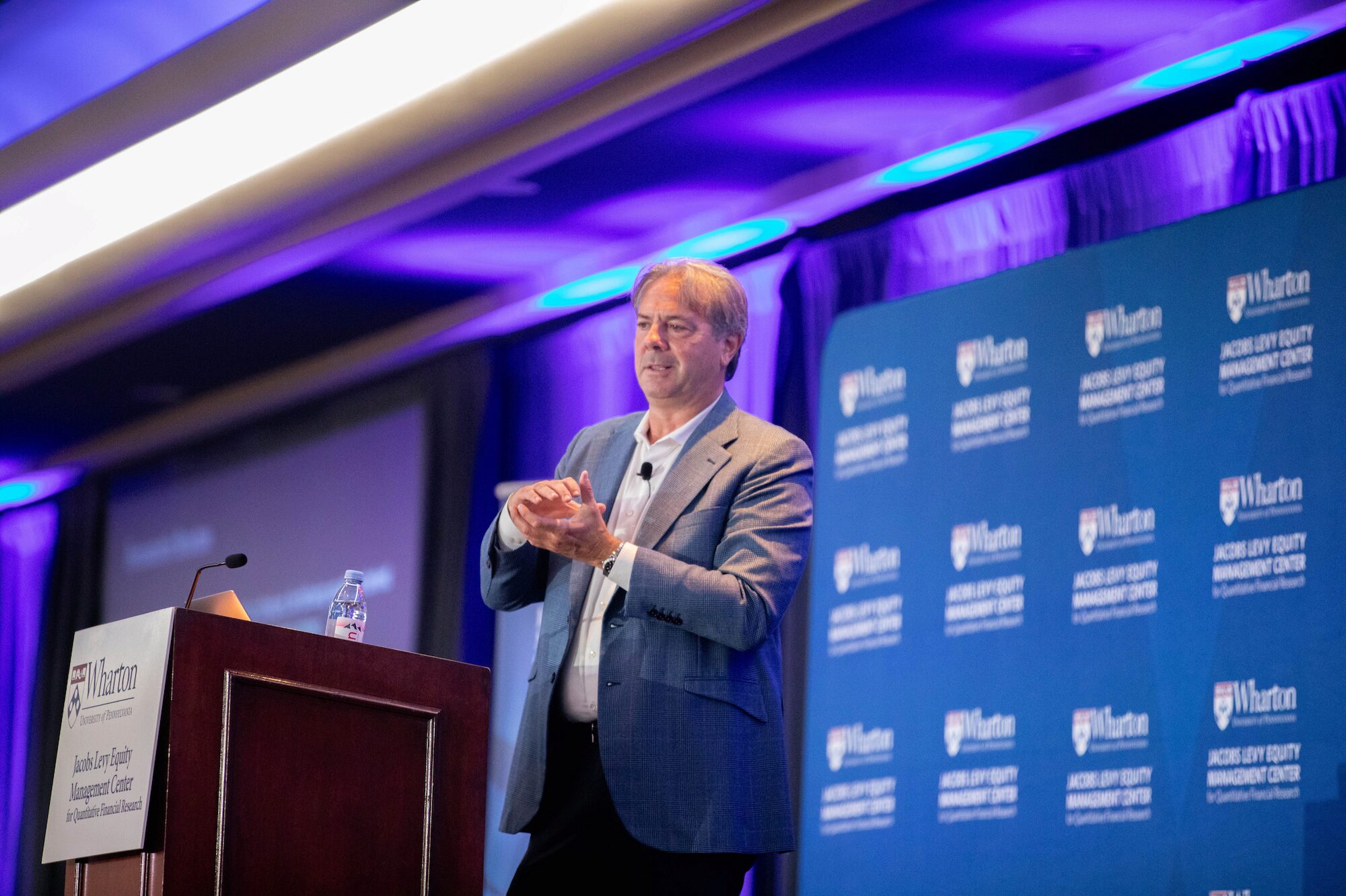 A conference speaker clasps his hands while giving a presentation from a podium