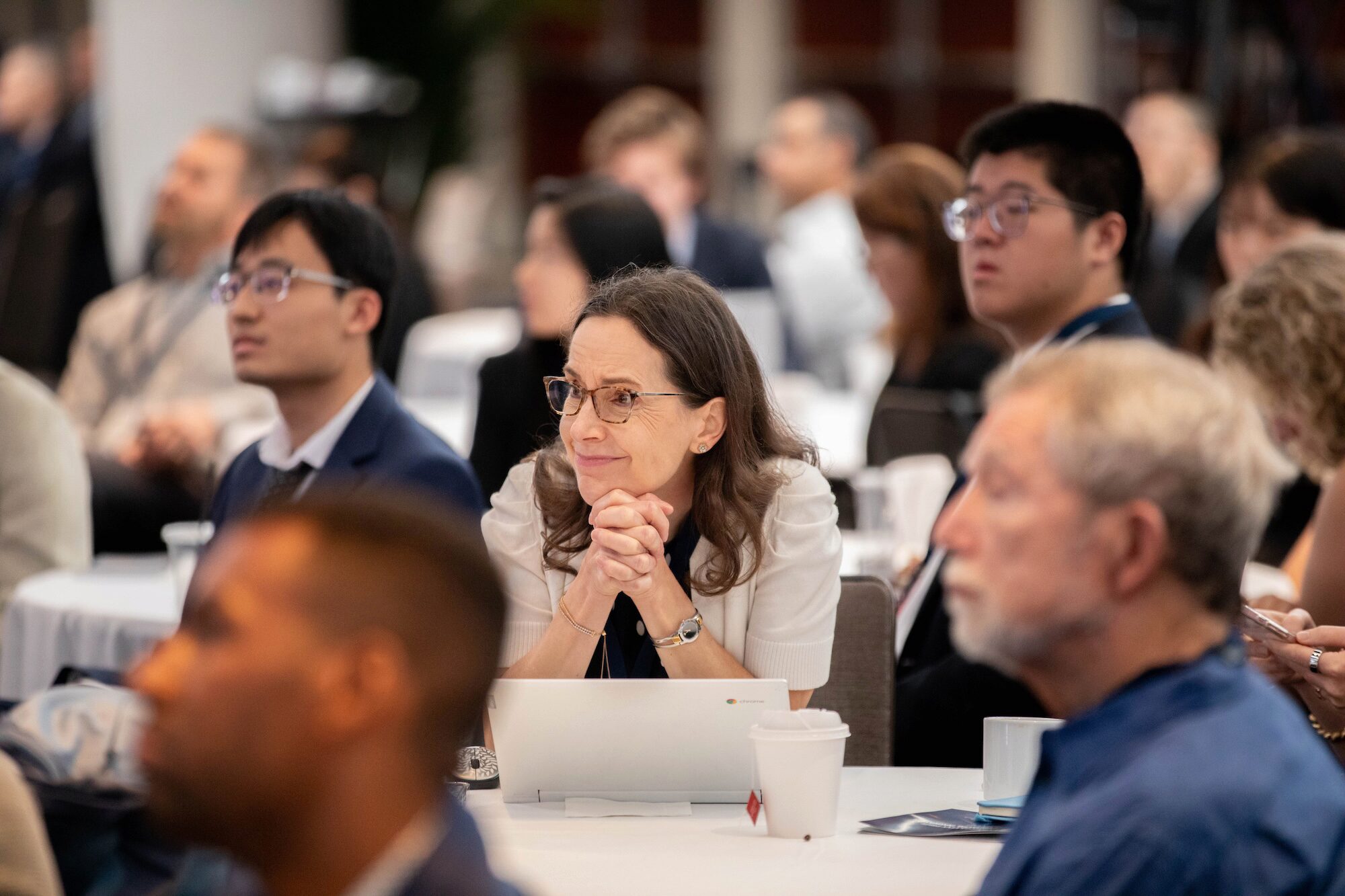 An audience watches a conference, seated at tables.