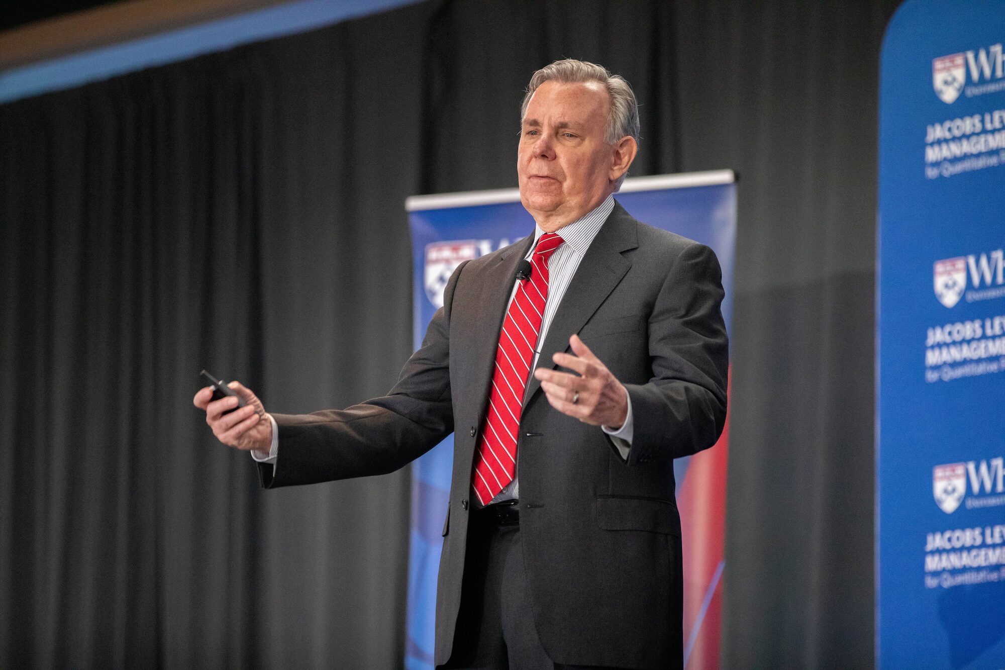 A conference speaker extends his arms outward while giving a presentation