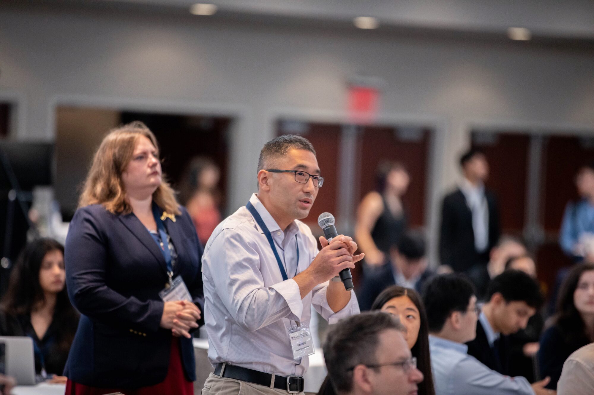 An audience member at a conference speaks into a microphone while in a crowd
