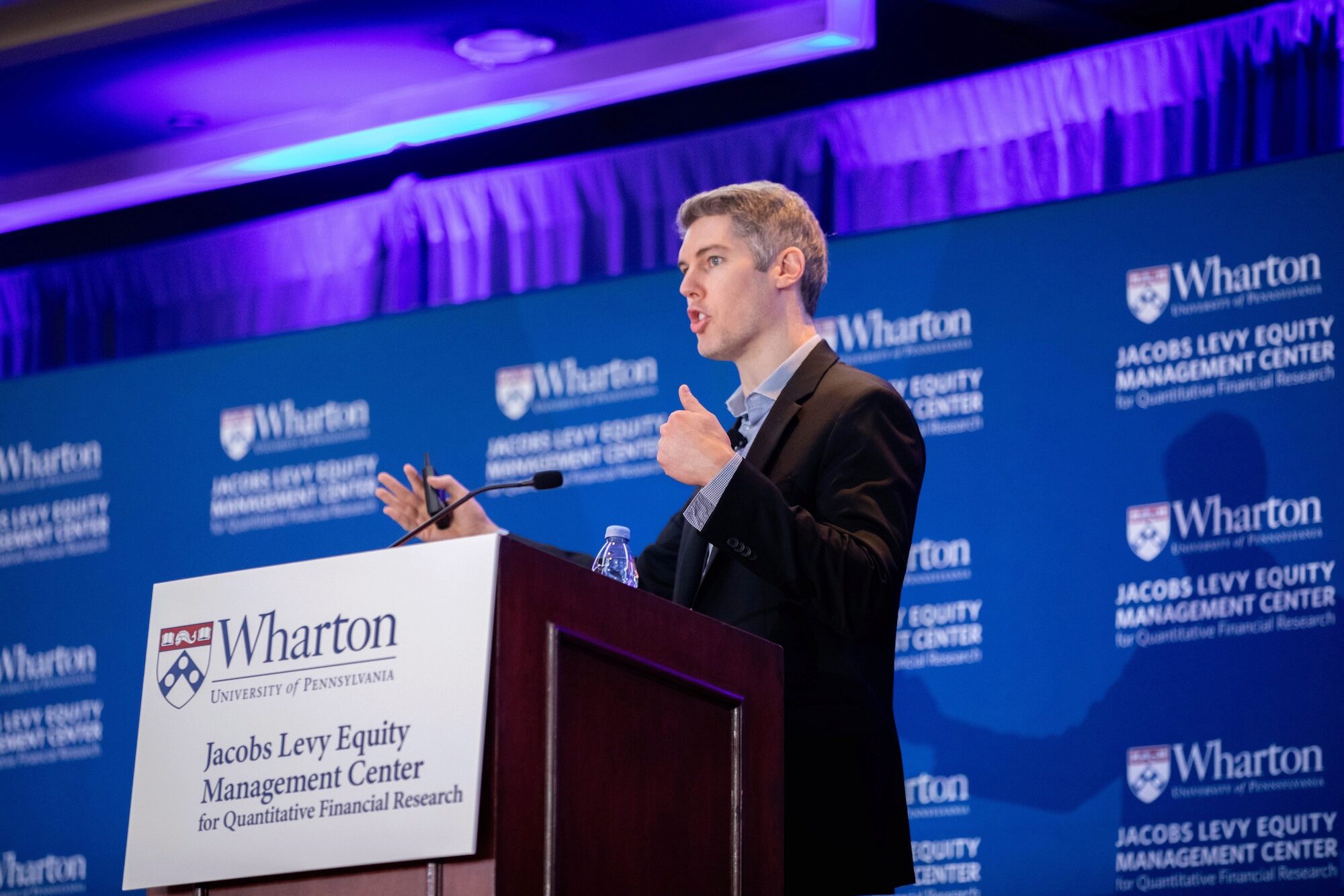 A person presents at a conference, speaking at a podium