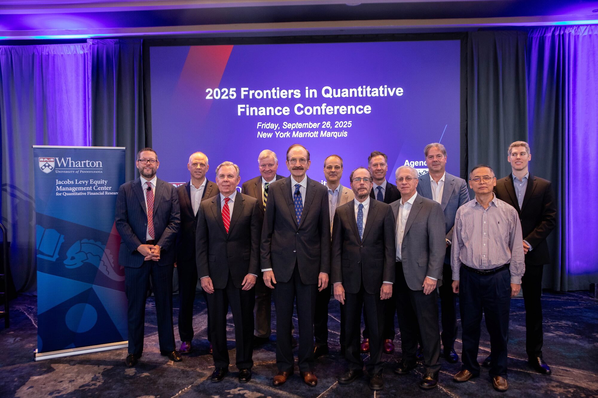 A group of people pose for a photo before a screen that reads, "2025 Frontiers in Quantitative Finance Conference"