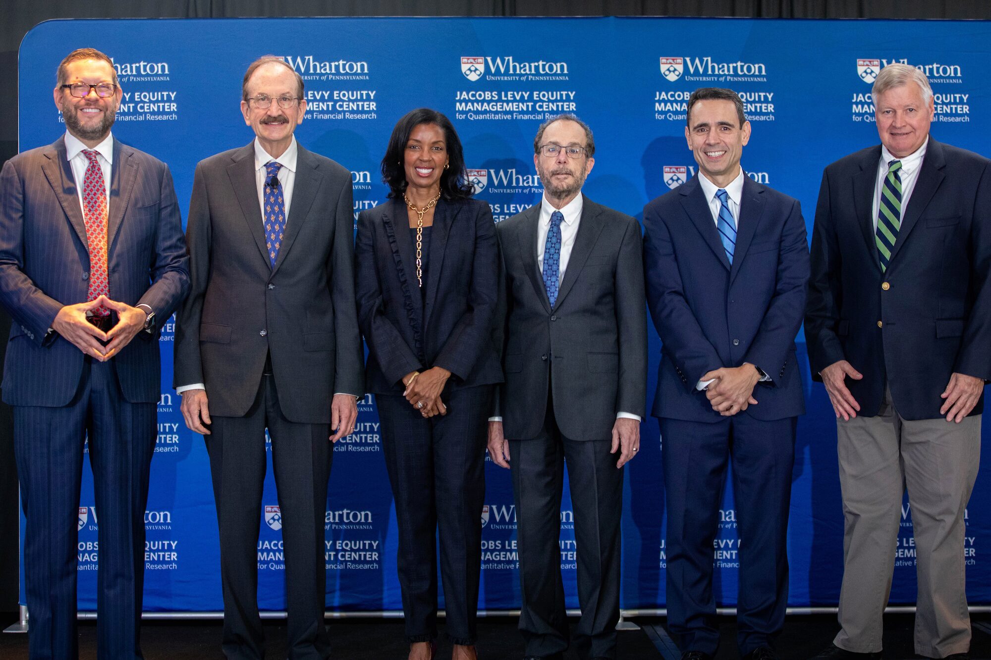 Six people pose for a group photo before a blue banner