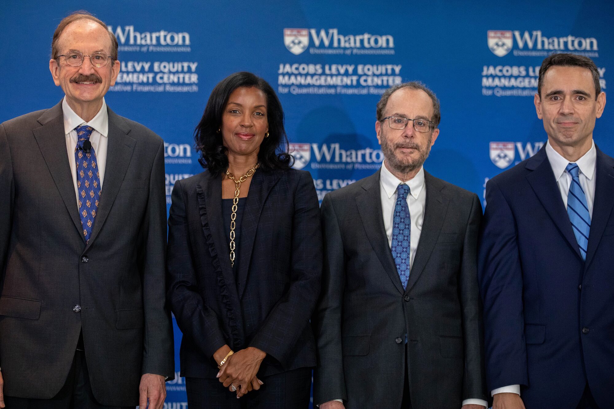 Four people pose for a group photo before a blue banner
