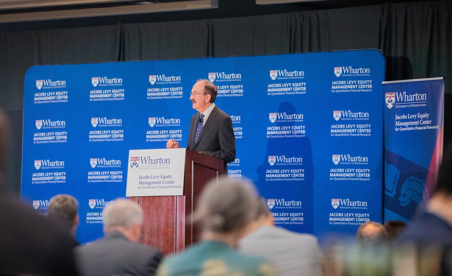 A conference speaker at a podium before a blue background