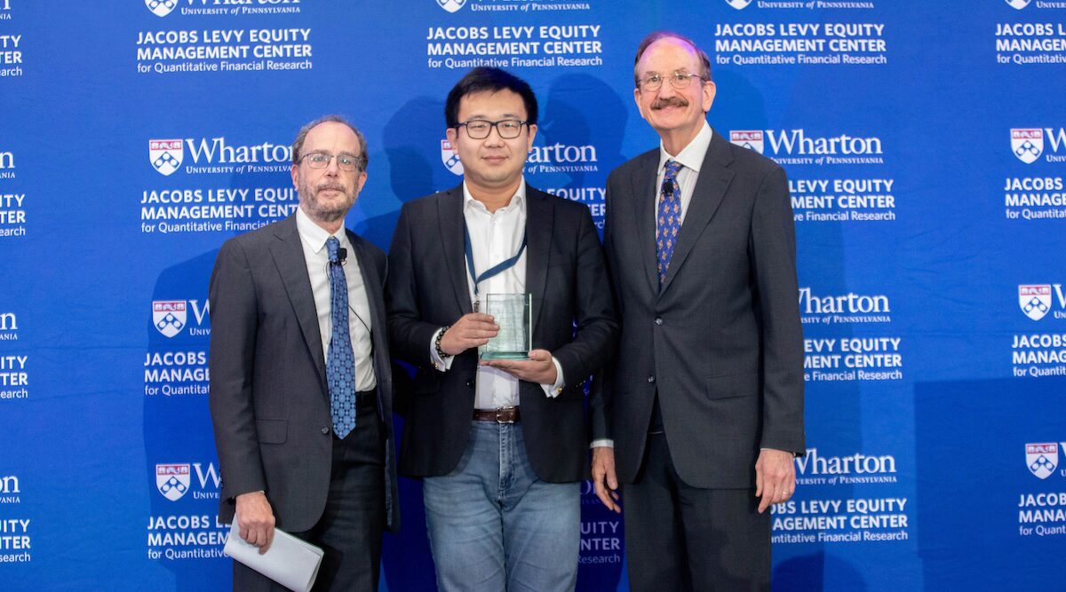 Three people pose for a group photo. The person in the middle holds a prize plaque.