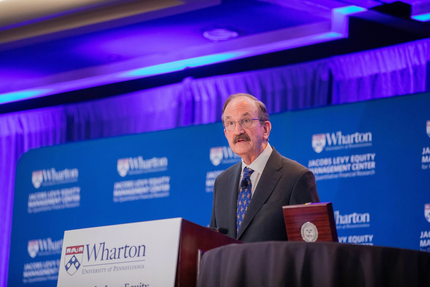 A conference speaker at a podium, with a wooden box opened beside him.