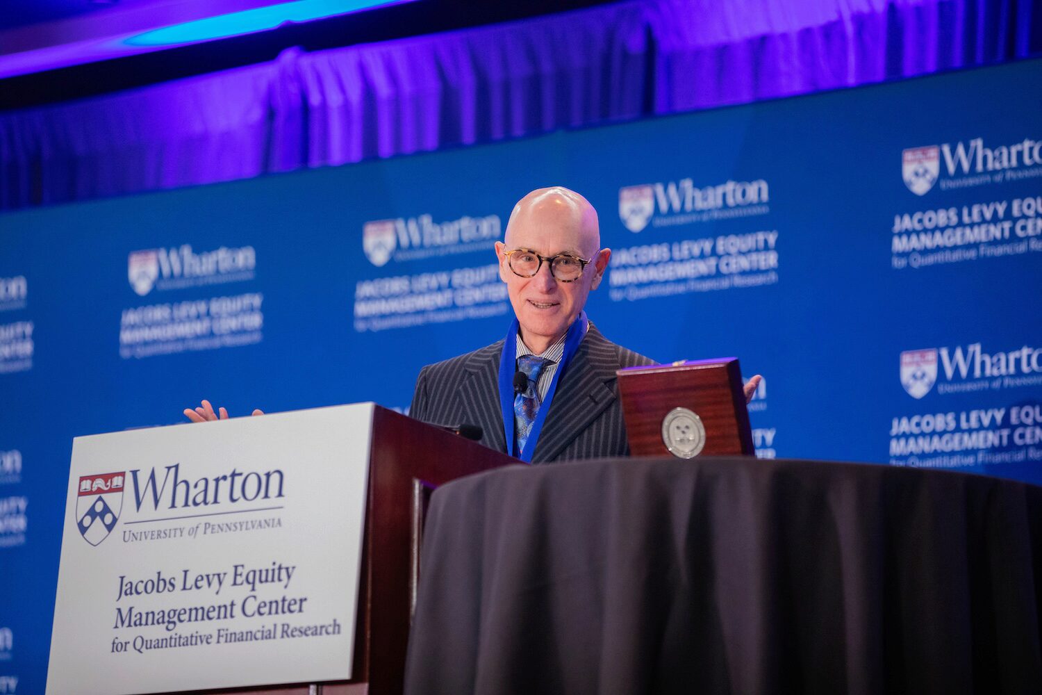 A person speaks from a podium. A wooden box is open beside him.