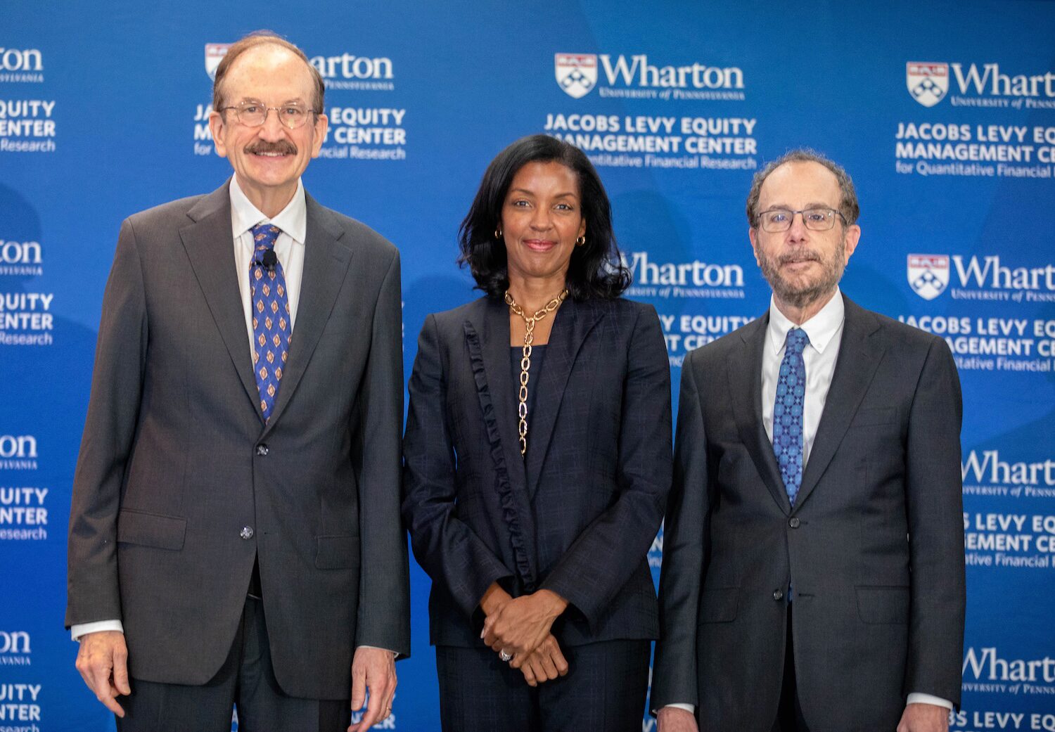 Three people pose for a group photo before a blue banner